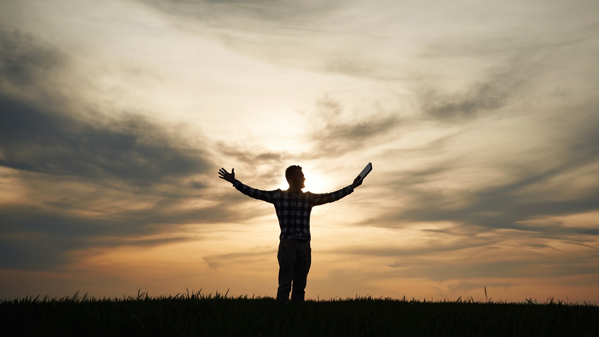 A man at sunset holding his arms out as if he's free.