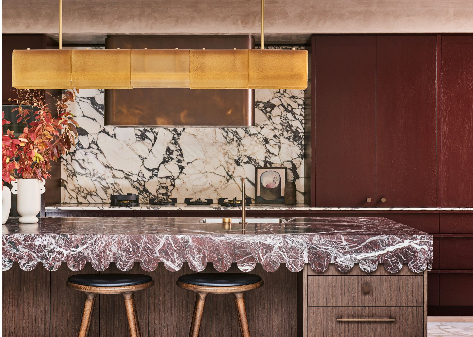 A kitchen with a fluted countertop in burgundy color, deep red cabinets, and a a gold-finished pendant light