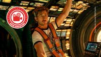 Project Hail Mary still. Ryan Gosling sits in a brightly lit space ship's interior, wearing an orange seatbelt with one hand pointed towards the roof.