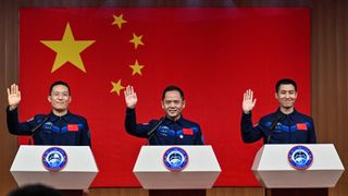 Three men wearing uniforms stand behind three podiums with a Chinese flag behind them