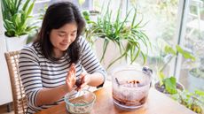 Woman sitting at table next to food processor bowl rolling a ball in her palms above a bowl of crushed nuts