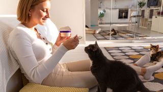 A woman eating yogurt while a cat watches