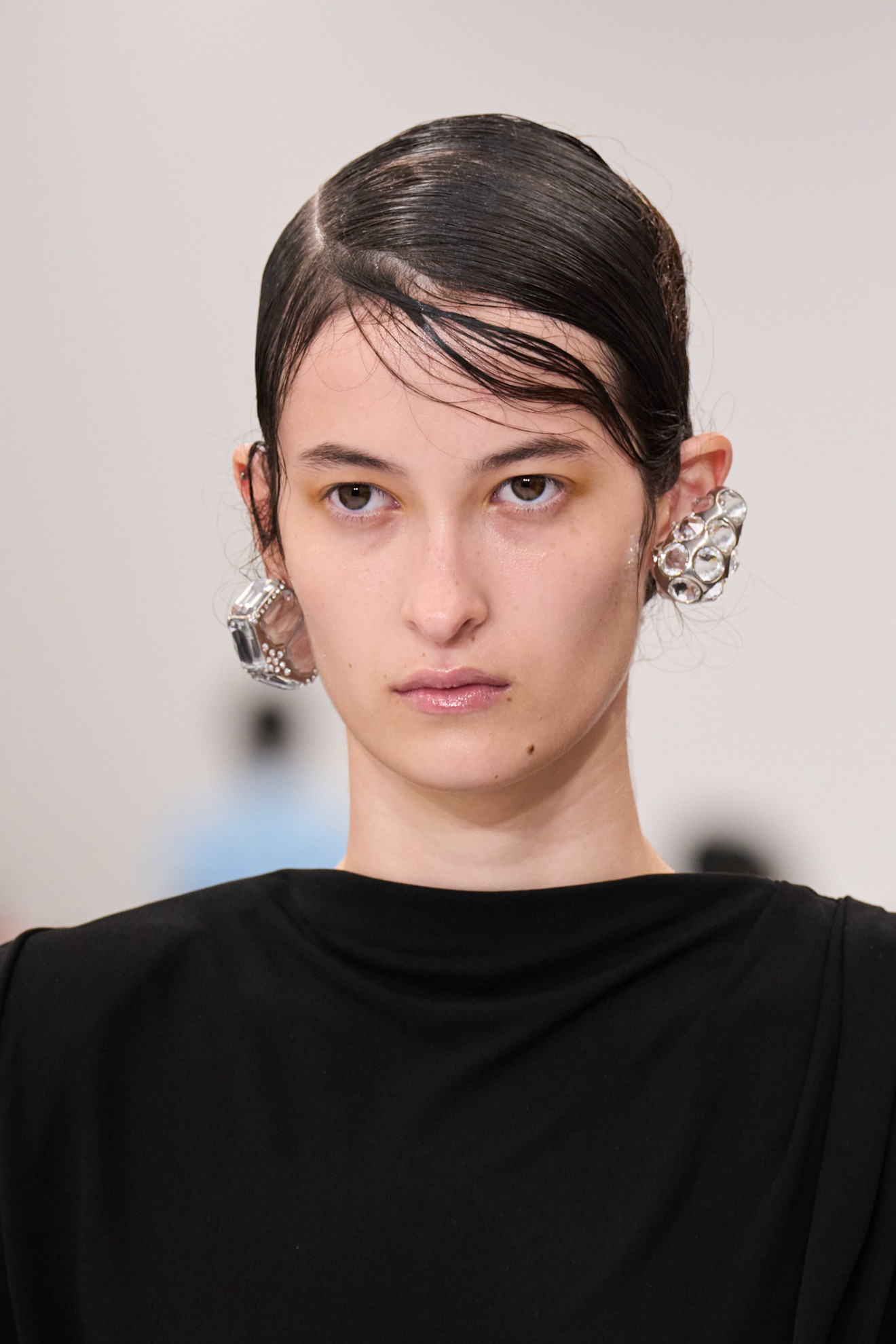 Acne Studios runway model wearing a plaid skirt, black top, and mismatched earrings.