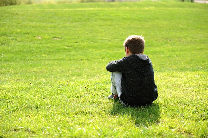 A boy sitting alone on the grass.