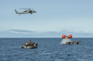 U.S. Navy personnel prepare to recover a mock Orion capsule from the sea.