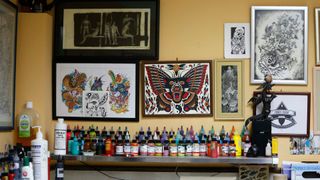 photo of rows of colorful tattoo inks in bottles displayed on a counter under framed traditional tattoo designs