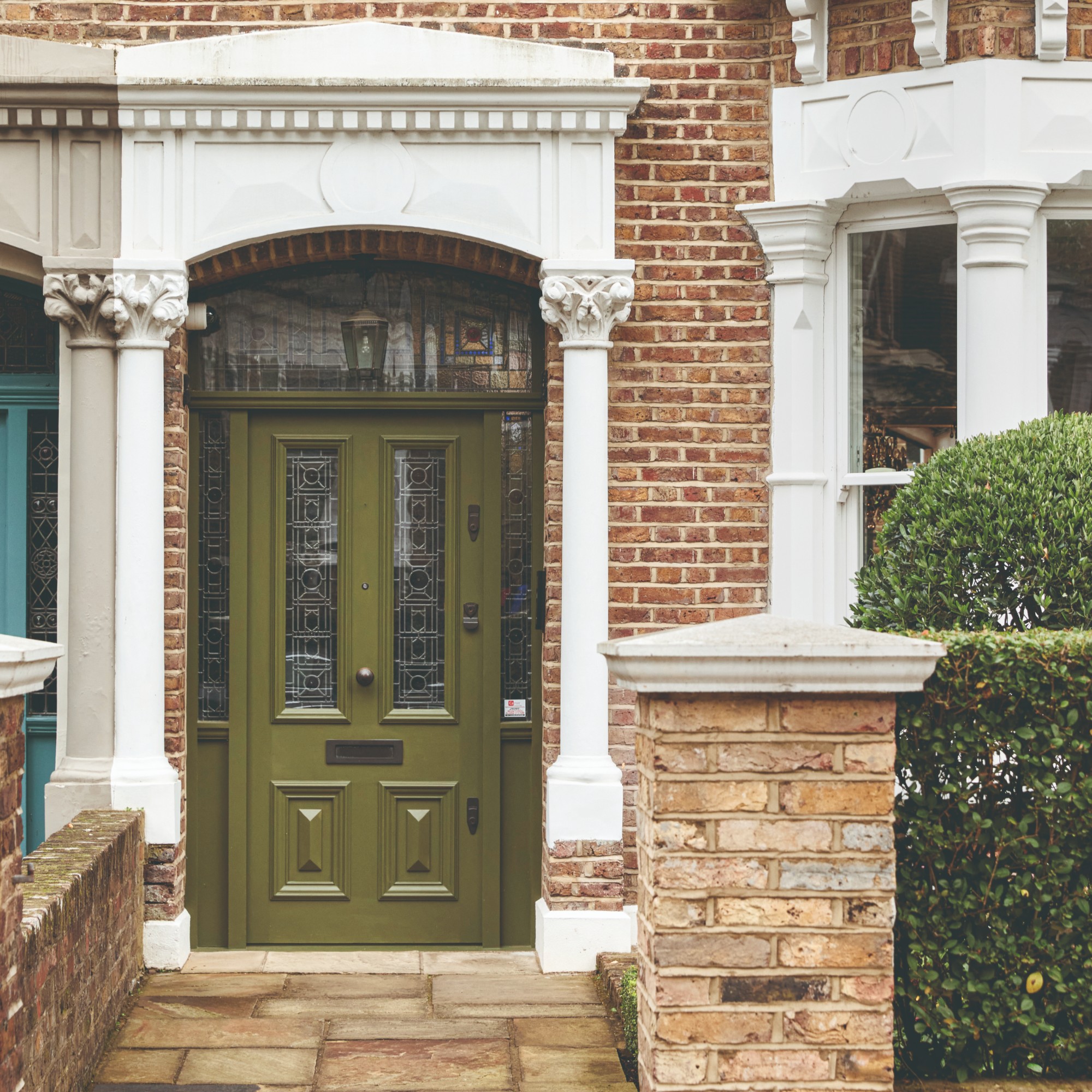 A front door painted in dark olive green with stained glass panels and a lantern pendant light