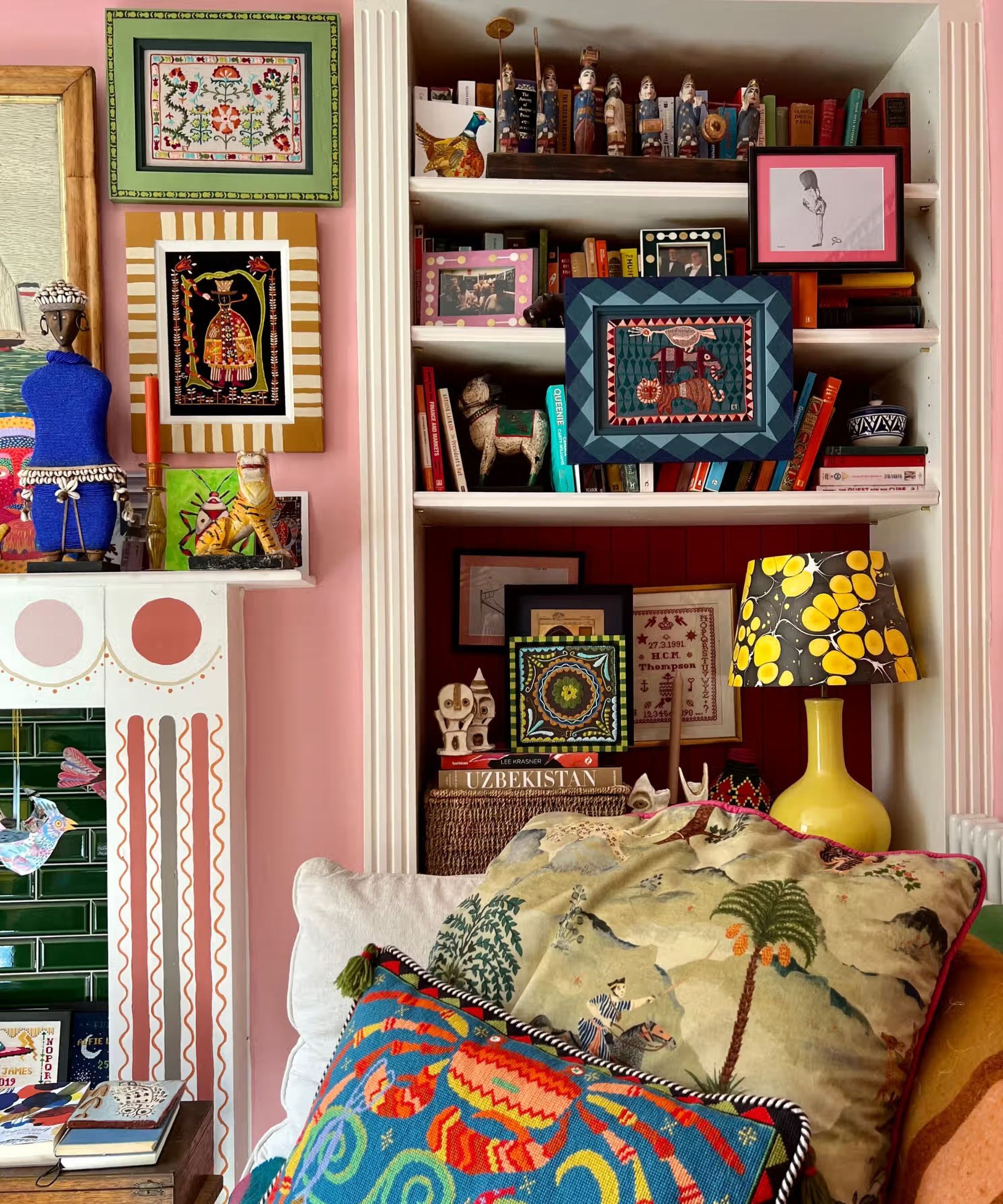 A pink sitting room with shelving, on the shelving are lots of boos, trinkets and decorative items including frames which have been handpainted