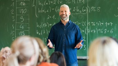 Mature teacher talking to students in front of blackboard covered in equations