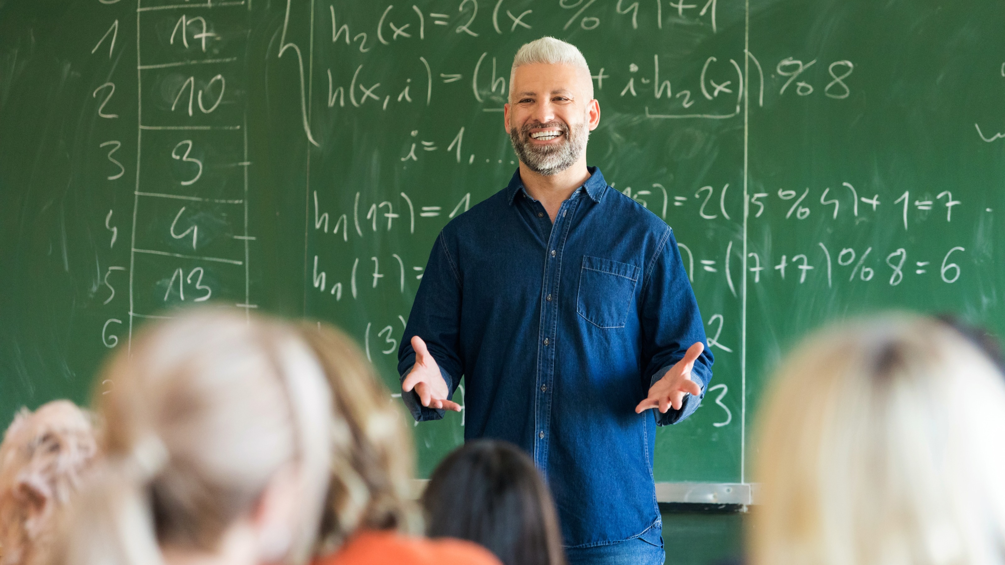 Mature teacher talking to students in front of blackboard covered in equations
