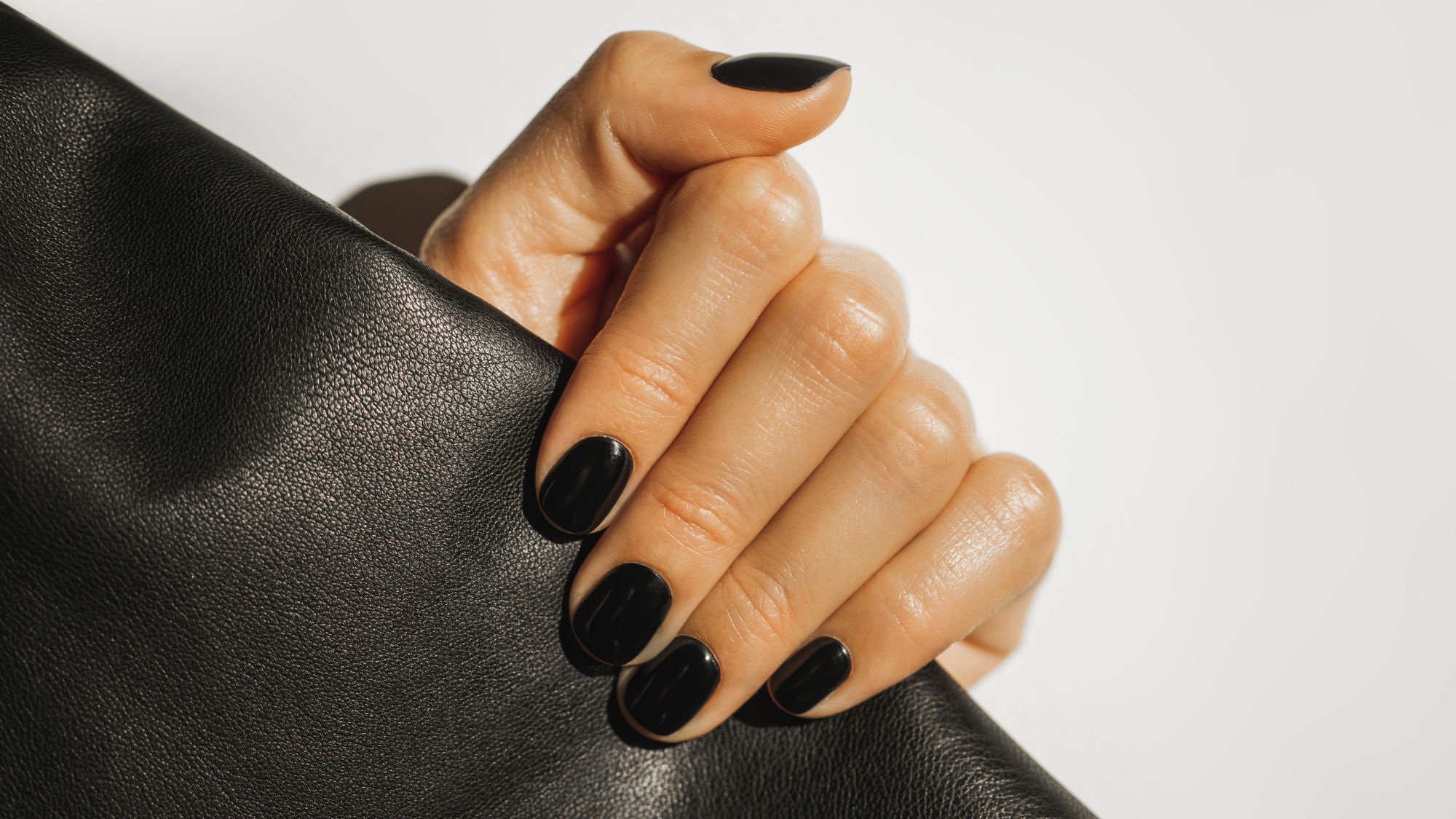 close up of a hand with a beautiful glossy black manicure holding onto a piece of black leather 