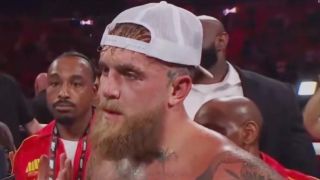 Jake Paul with a white ball cap on backwards listening to Ariel Helwani after his fight with Anthony Joshua