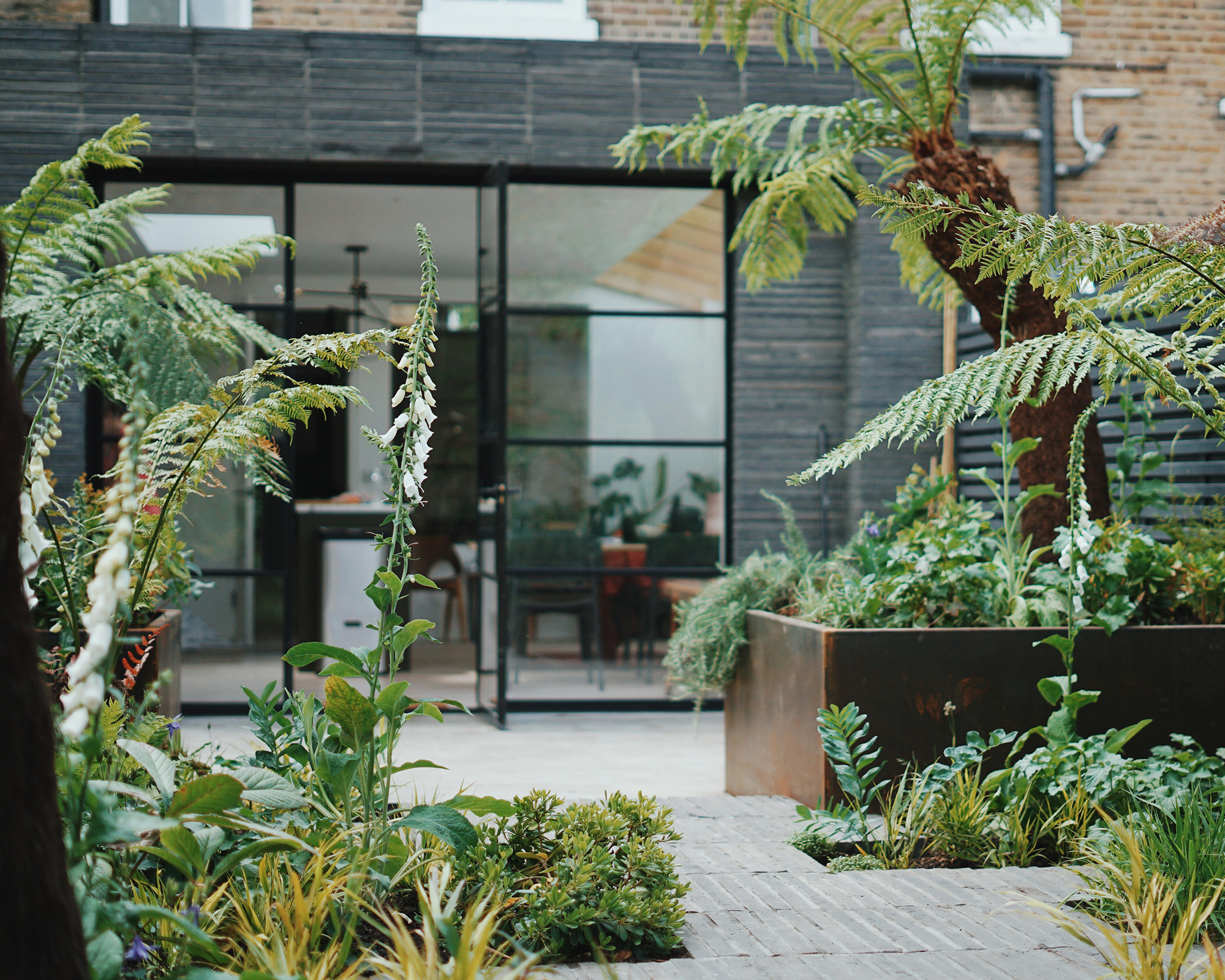 a backyard terrace area with corten steel planters and crittal patio doors