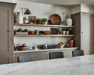 An example of small kitchen storage ideas showing open shelving storing plates, crockery and vases in between two stone colored cabinets