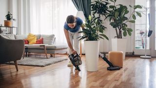 Woman cleaning a hardwood floor with a handheld vacuum and cordless vacuum