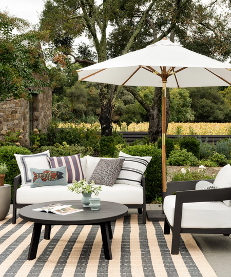 a patio space with black outdoor furniture with white cushions, decorative pillows, and a white umbrella