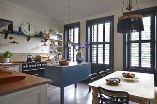 Designing a kitchen island with a blue freestanding unit in a cream and wood scheme with blue window frames and shutters.