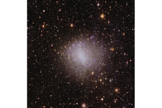 A sparkly pinkish and white blob of light in the center of the image, surrounded by a millions of light specks representing distant cosmic objects.