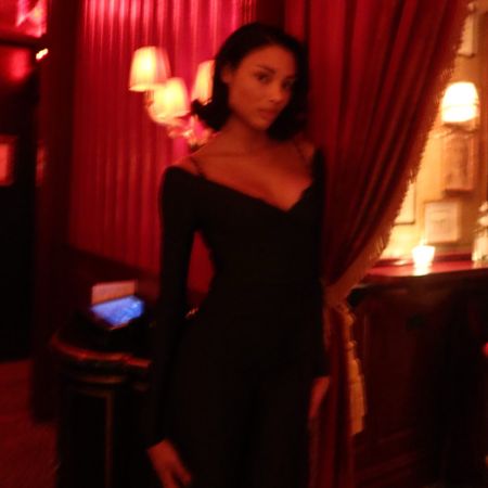 Woman wearing a black dress in a dark, red-velvet-covered bar