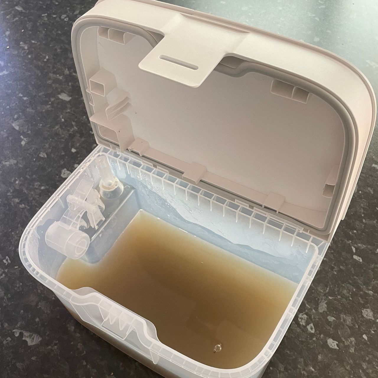 Brown water inside a robot vacuum dirty water tank, on grey worktop