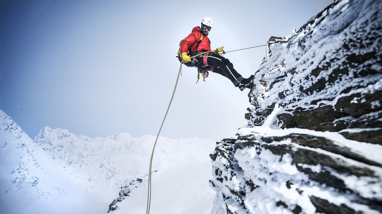 A mountain climber descends a snowy peak while using a rope.