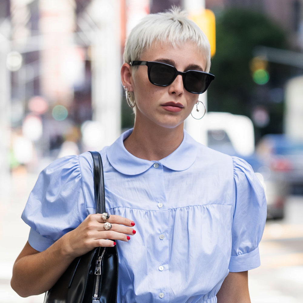 Emma Chamberlain wearing a blue romper, black leather bag, and black sunglasses in NYC 