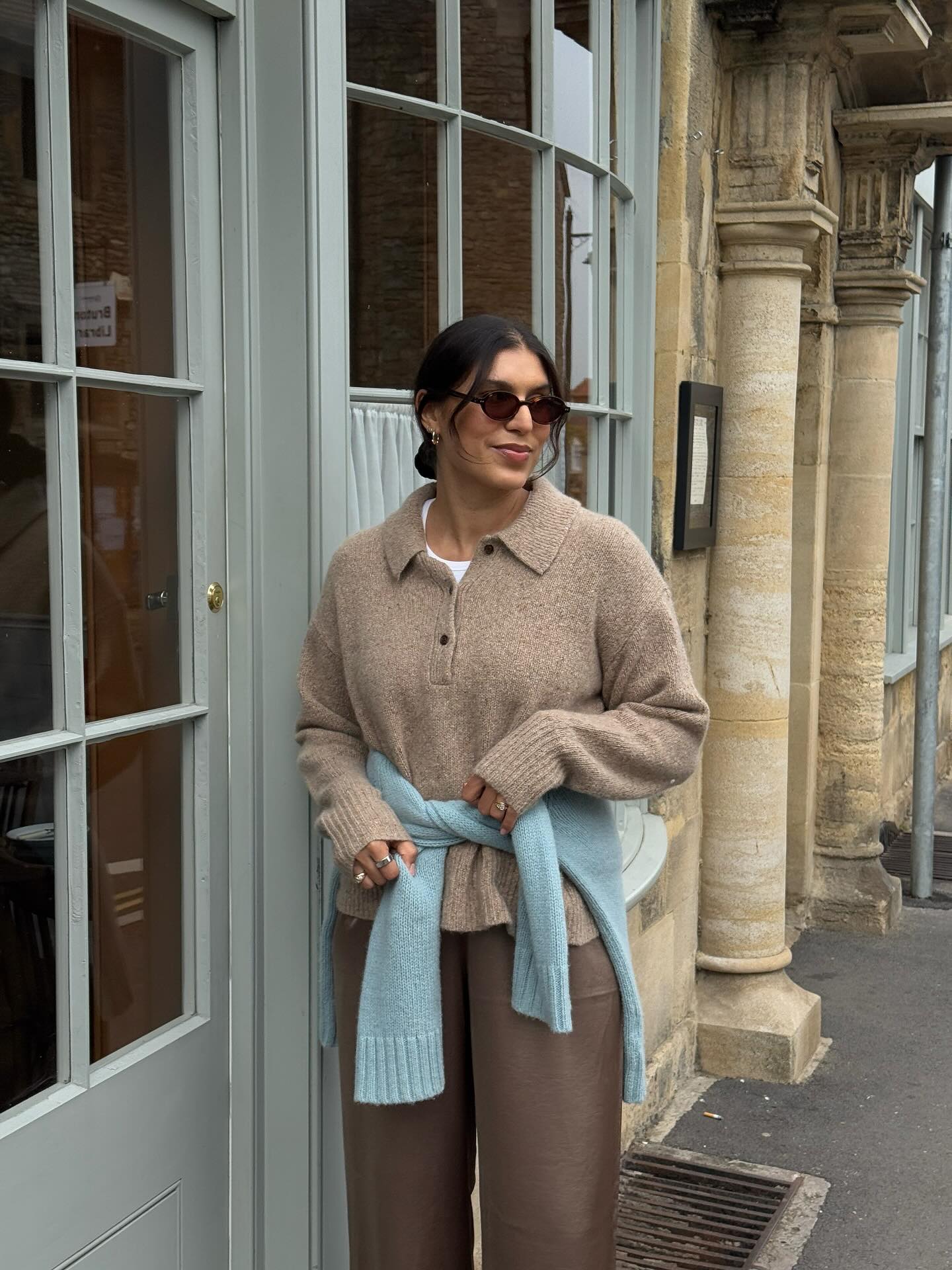 An image of @theindiaedit wearing a taupe knit polo with a sky blue cardigan, one of the leading colour trends of 2025.