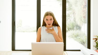 A female worker at her desk looks happily surprised while looking at her laptop.