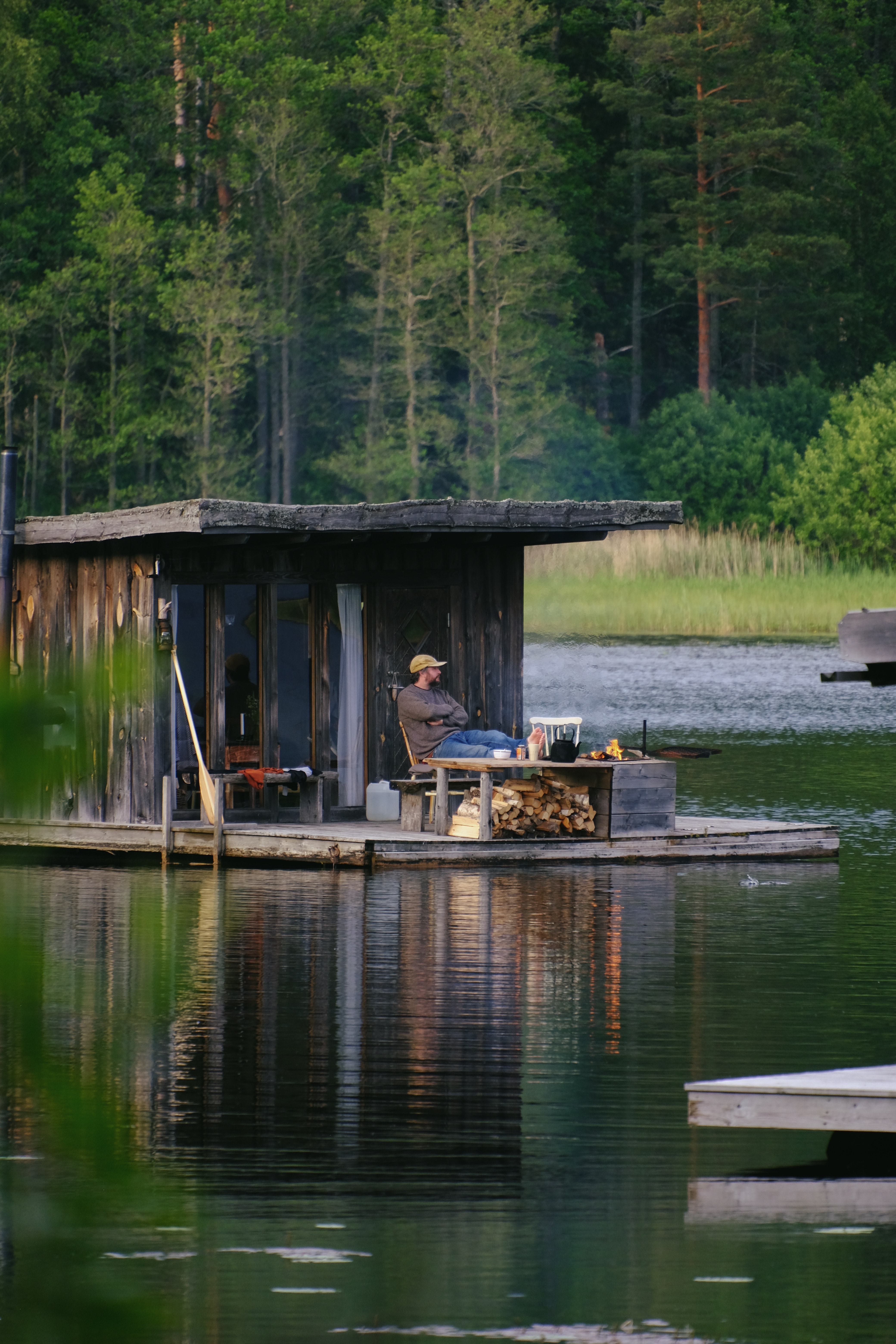 A man sit on the deck of a floating wood powered sauna in the middle of a lake in Sweden