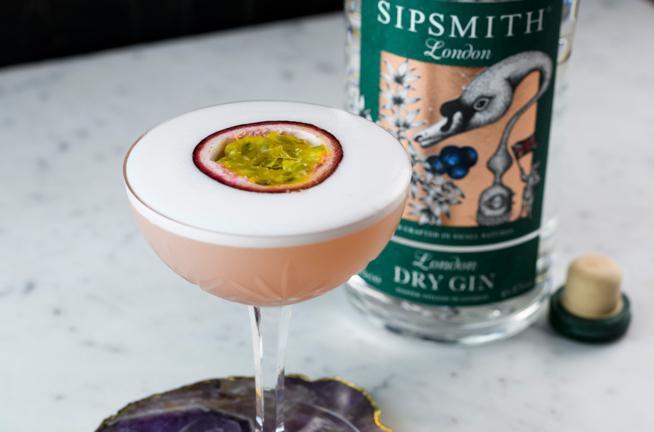 A pink Martini with a slice of passionfruit in front of a bottle of gin