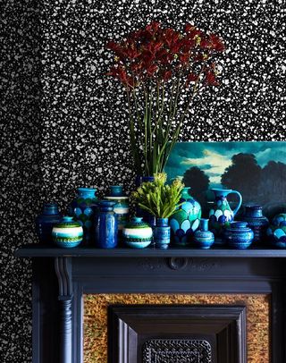 black and white wallpaper behind blue painted mantle with an assortment of blue pottery