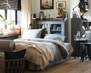 A bedroom in a living room with cabinetry and black out blinds