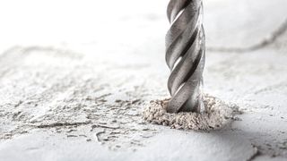 Close up of silver drill bit drilling into concrete