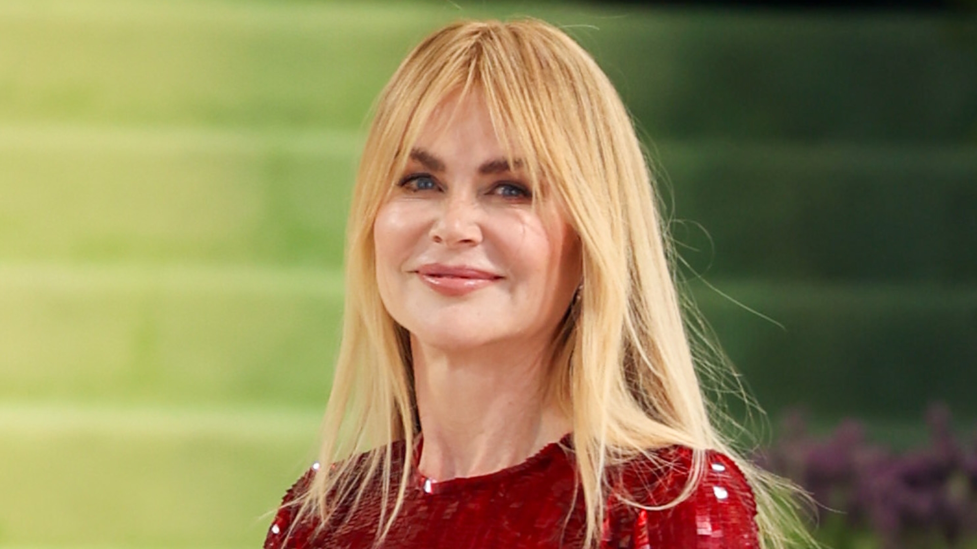 Image of Nicole Kidman smiling at the Met Gala 2026, with golden blonde straight hair and fringe, wearing a red sequin gown