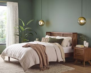 bedroom with sage green walls, neutral bedding, rattan headboard and wood nightstand and brass pendant lights