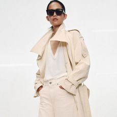 Model wears cream trench coat, white top and cream jeans