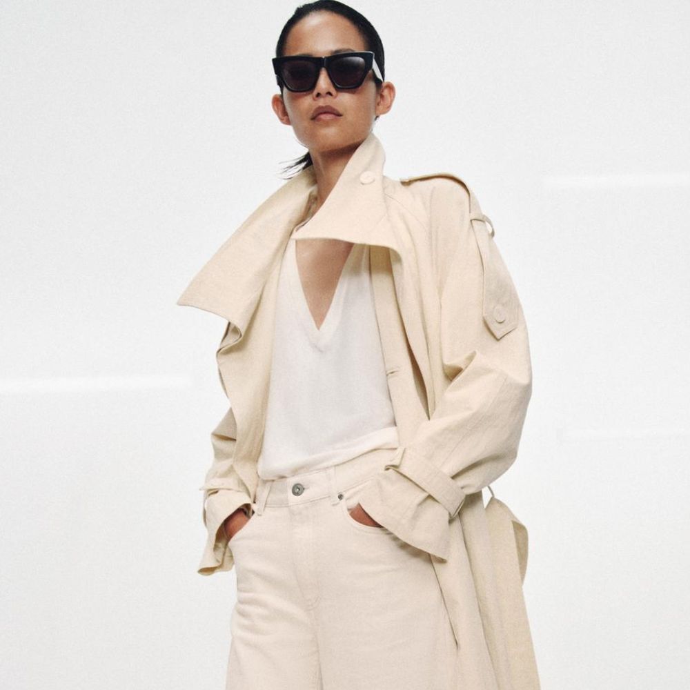 Model wears cream trench coat, white top and cream jeans