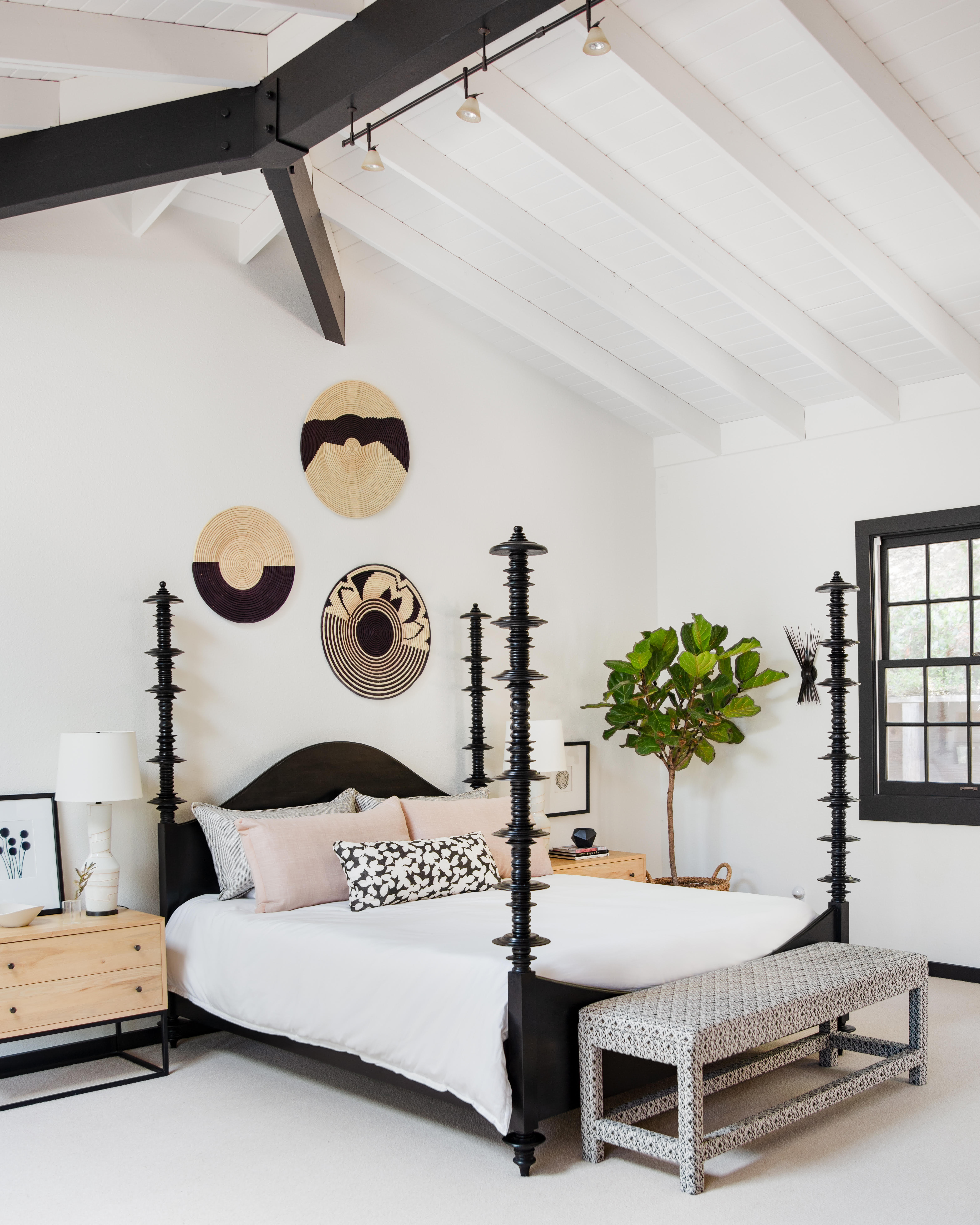 white bedroom with black statement bed, pale wood bedside tables, pink cushions, white lamps, white carpet