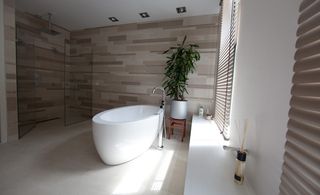 Bathroom with oval shaped ceramic bath and glass enclosed shower space. Grey window blinds