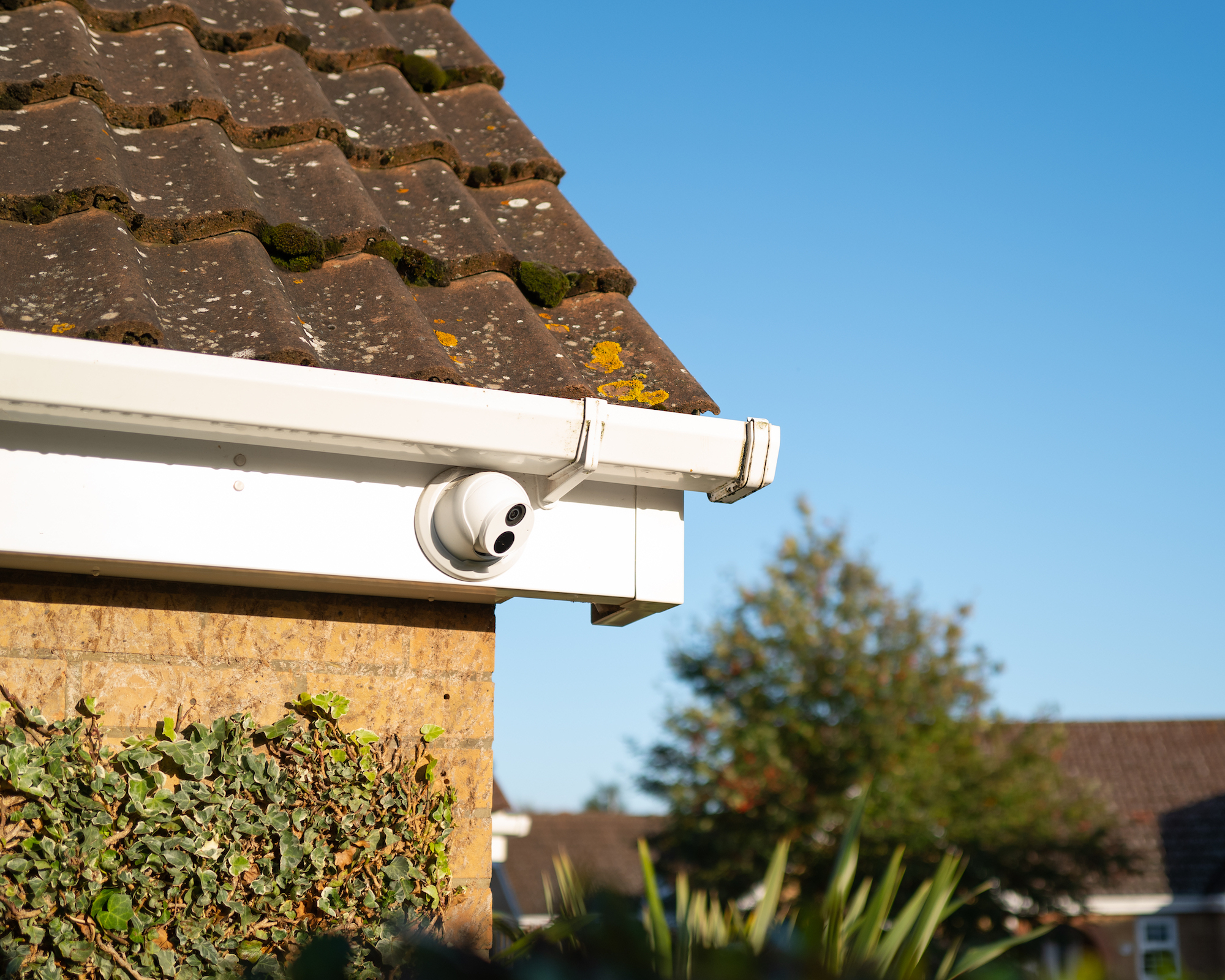 CCTV camera attached to the eaves of a bungalow with house beyond