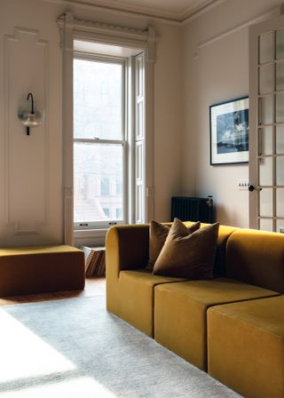 Living room with warm beige walls and ochre sofa and footstool