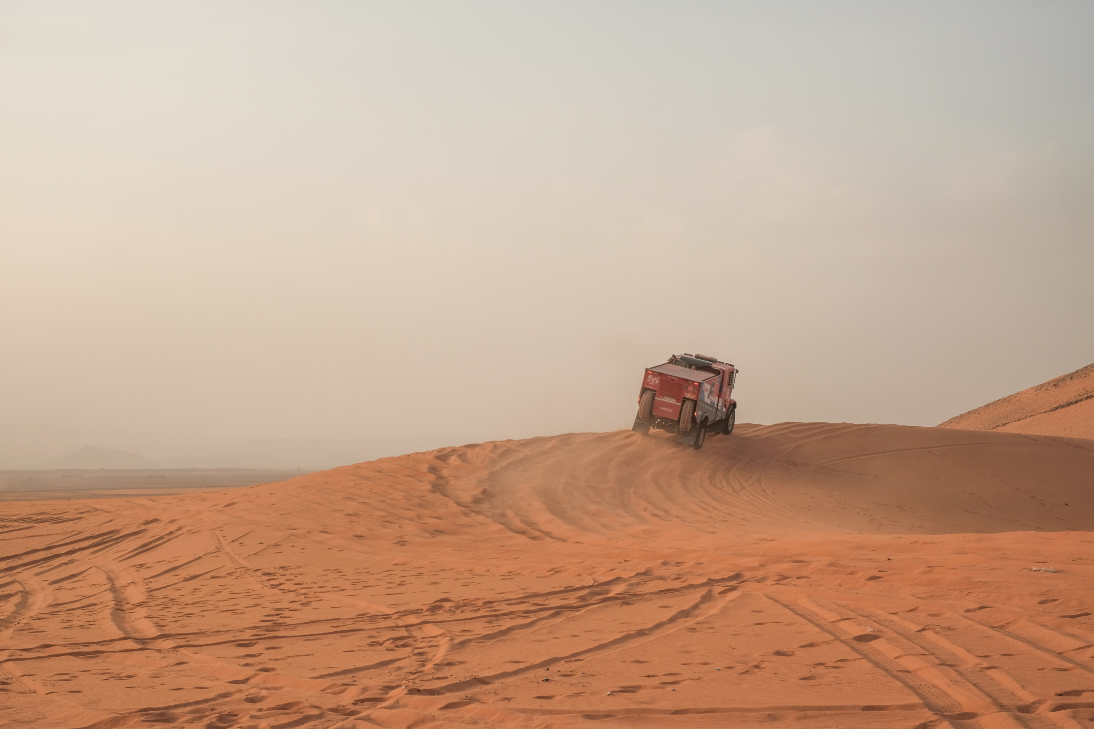 A Dakar Rally lorry crests a dune in the distance, heading out to the desert