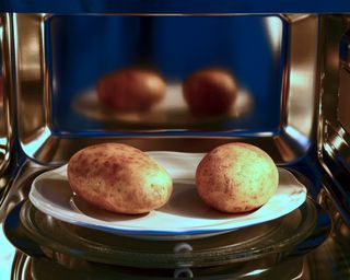 Two white potatoes being cooked inside a microwave oven appliance