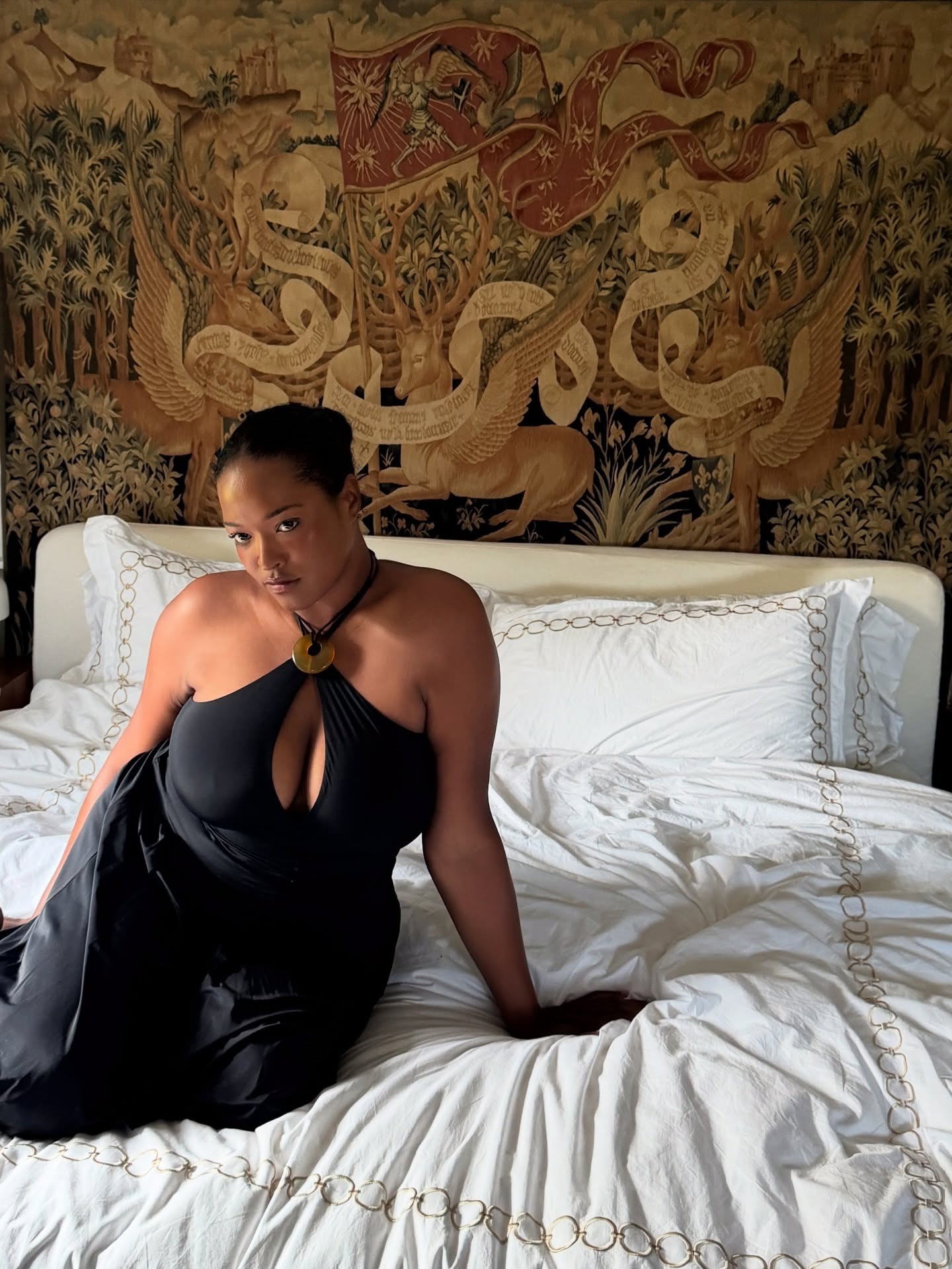 Photo of creator @_imanirandolph wearing a black dress on a hotel room bed
