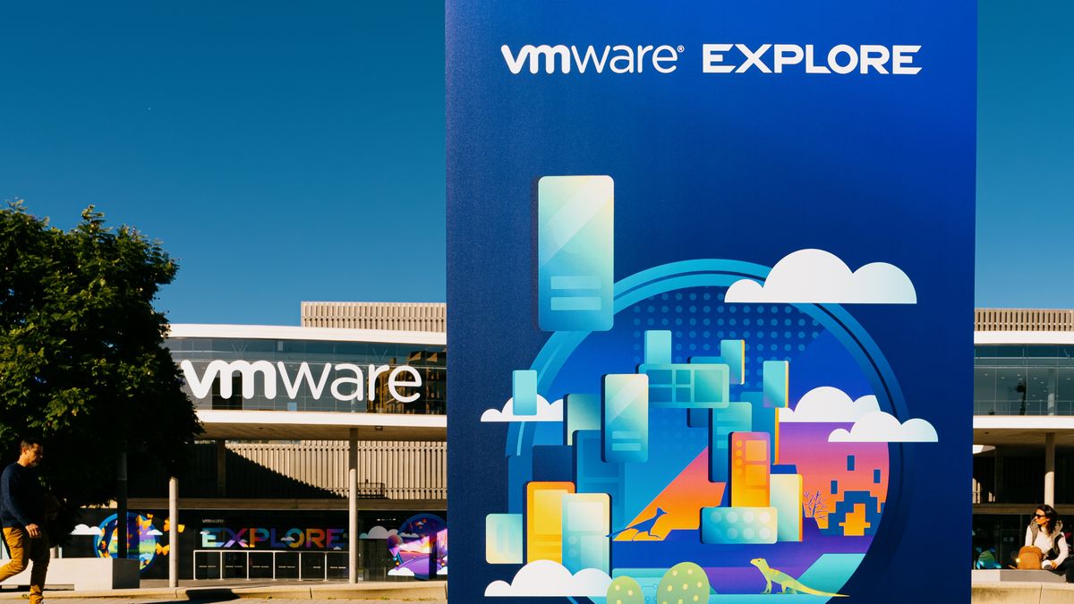 The VMware Explore logo on a sign with clouds, with the Fira Barcelona conference center in the background with the VMware logo on it.