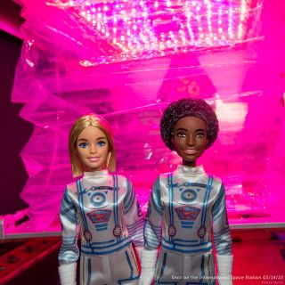 Mattel's two Mission DreamStar Barbie dolls are photographed in front of the Veggie plant growth facility on the International Space Station.