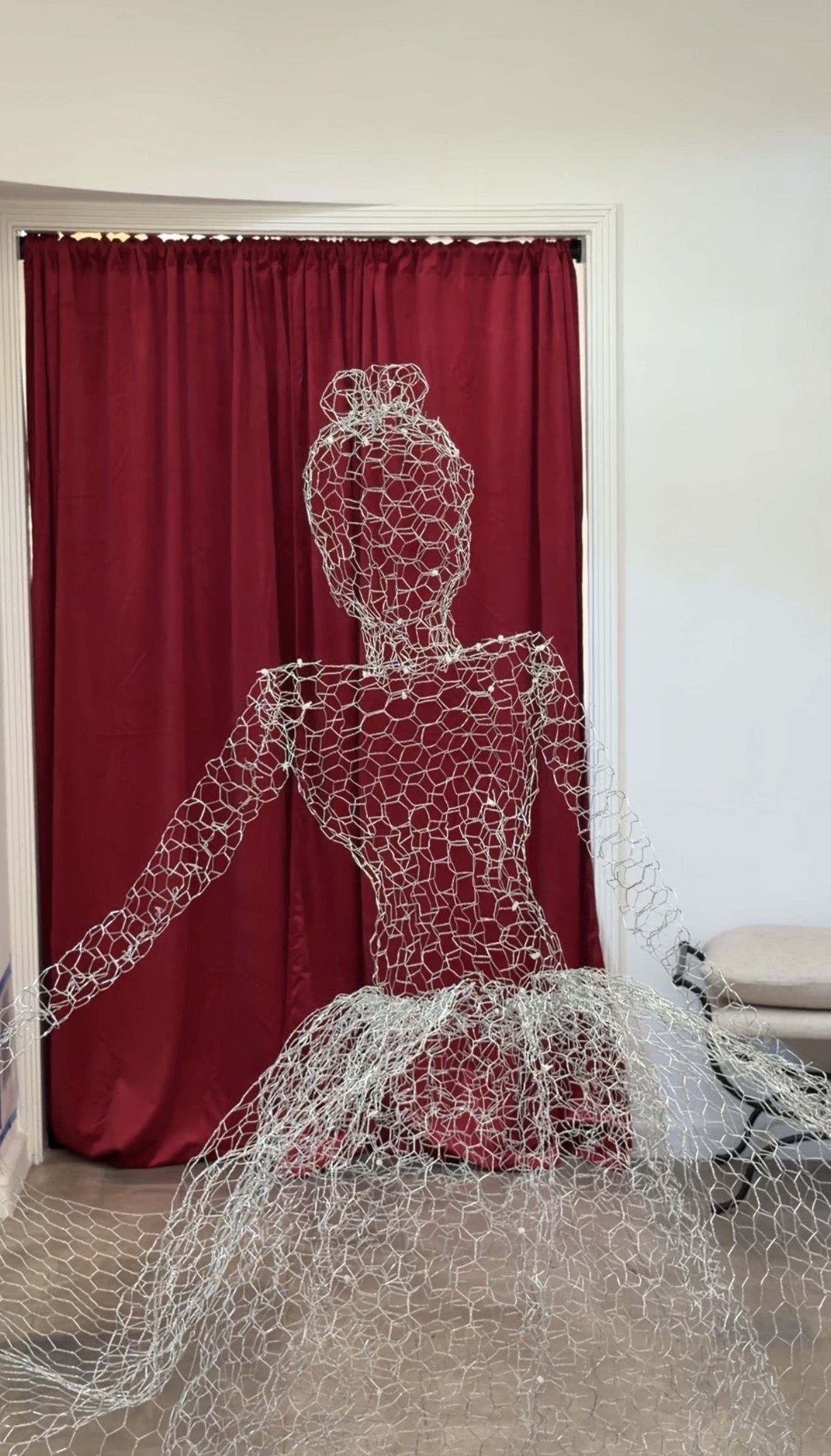 A chicken wire ghost dancer in front of a red velvet curtained doorway
