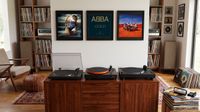 Three turntables on a media unit, with some records hanging on a wall behind.