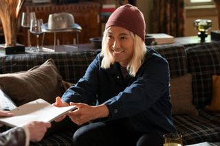 Jin Ha as Marshall/Rex, reaching with both hands for a script as he sits on a couch, in 'Only Murders in the Building' season 4.