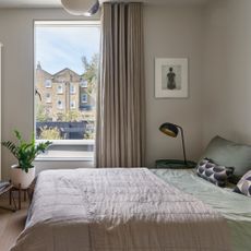 A neutral bedroom with taupe curtains and sage green and taupe bedding